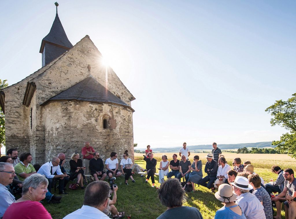 Sitzkreis mit Menschen vor einer alten Kirche