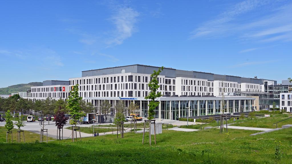 Großes weißes Klinikgebäude mit Parkflächen und grüner Wiese im Vordergrund.
