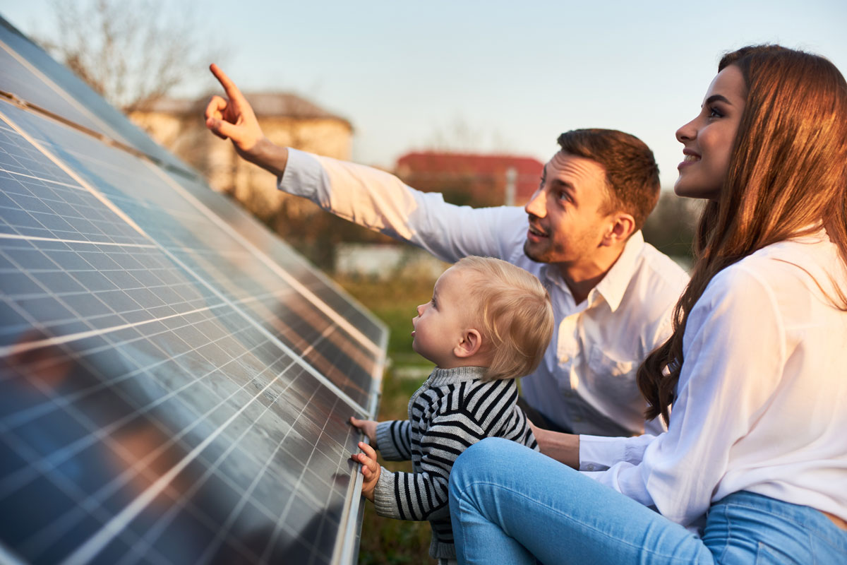 junge Familie mit Kleinkind begutachtet stolz ihre neue Photovoltaikanlage auf einer Wiese