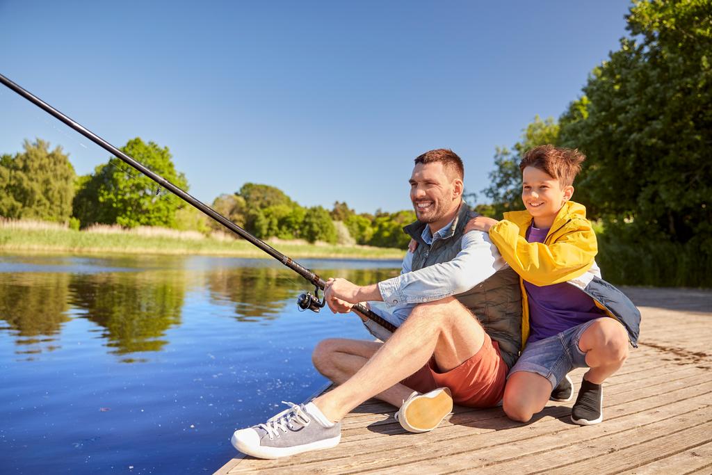 Vater mit Sohn sitzen auf Bootssteg am See und angeln.