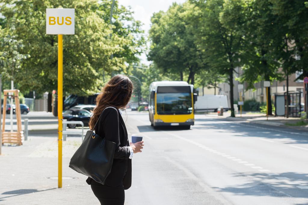 Eine junge Frau steht an der Haltestelle und wartet auf den Bus