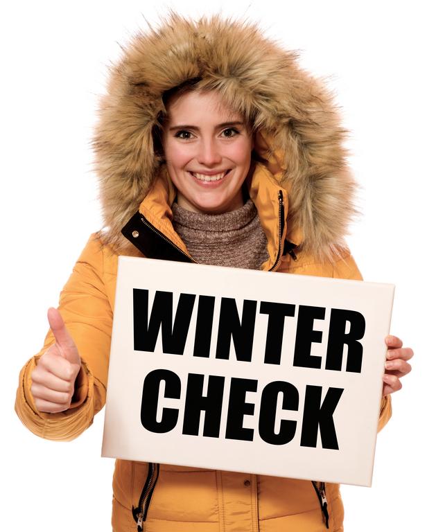 Frau mit dicker Winterjacke lächelt. In der linken Hand hält sie eine Tafel mit der Aufschrift "Wintercheck", die rechts Hand streckt sie mit Daumen hooch in die Höhe.