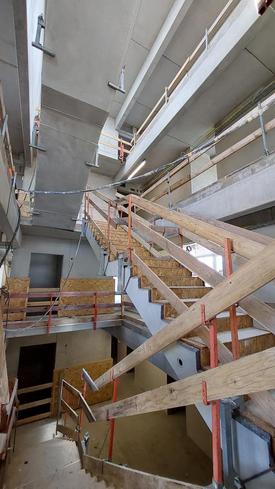 Ein im Bau befindliches offenes Treppenhaus über mehrere Etagen. Das Geländer besteht aus provisorischen Baubrettern.