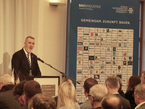 Bauminister Steffen Schütz hält zur Jahresauftaktveranstaltung der Bauwirtschaft eine Rede. Er steht an einem Pult vor sitzenden Personen und spricht.