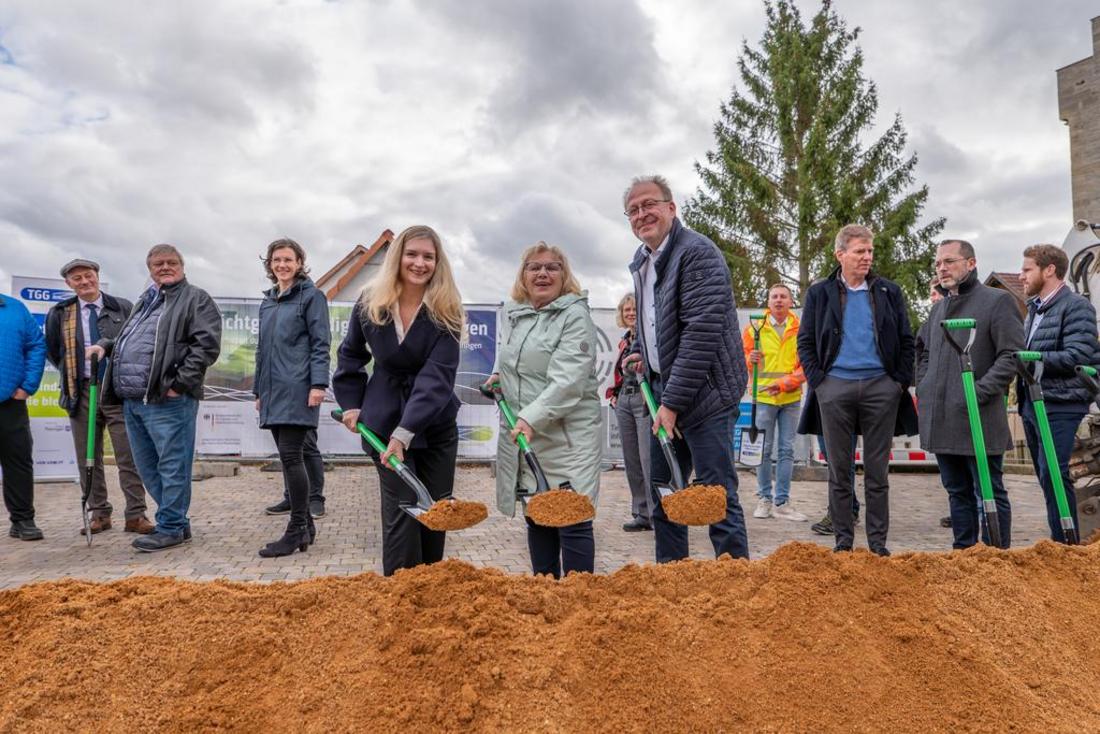 Die Staatssekretärin Milen Starke steht mit weiteren Personen an einem großen Sandhaufen mit einer Schaufel anlässlich des Symbolischen Spatenstichs für die Glasfaseranbindung in Bauerbach