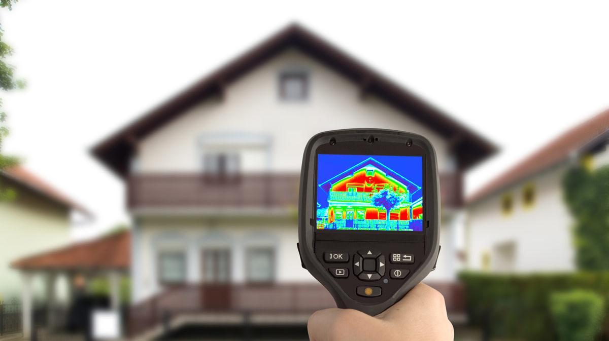 Closeup Wärmbildkamera wird auf Haus gerichtet, das Haus ist unscharf im Hintergrund zu sehen