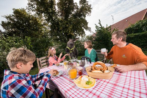 Familie sitzt im Garten eines Dorfes am Holztisch mit regionalen Produkten