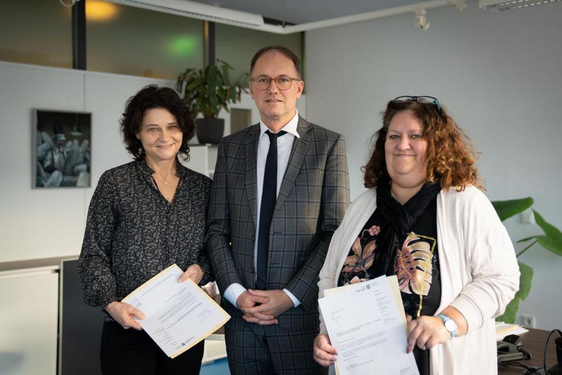 drei Personen, in der Mitte Staatssekretär Dr. Knoblich, stehen nebeneinander. Die beiden Frauen halten Ihre Mitteilungen über ihre Wahl zur Gleichstellungsbeauftragten und stellvertretenden Gleichstellungsbeauftragten in den Händen