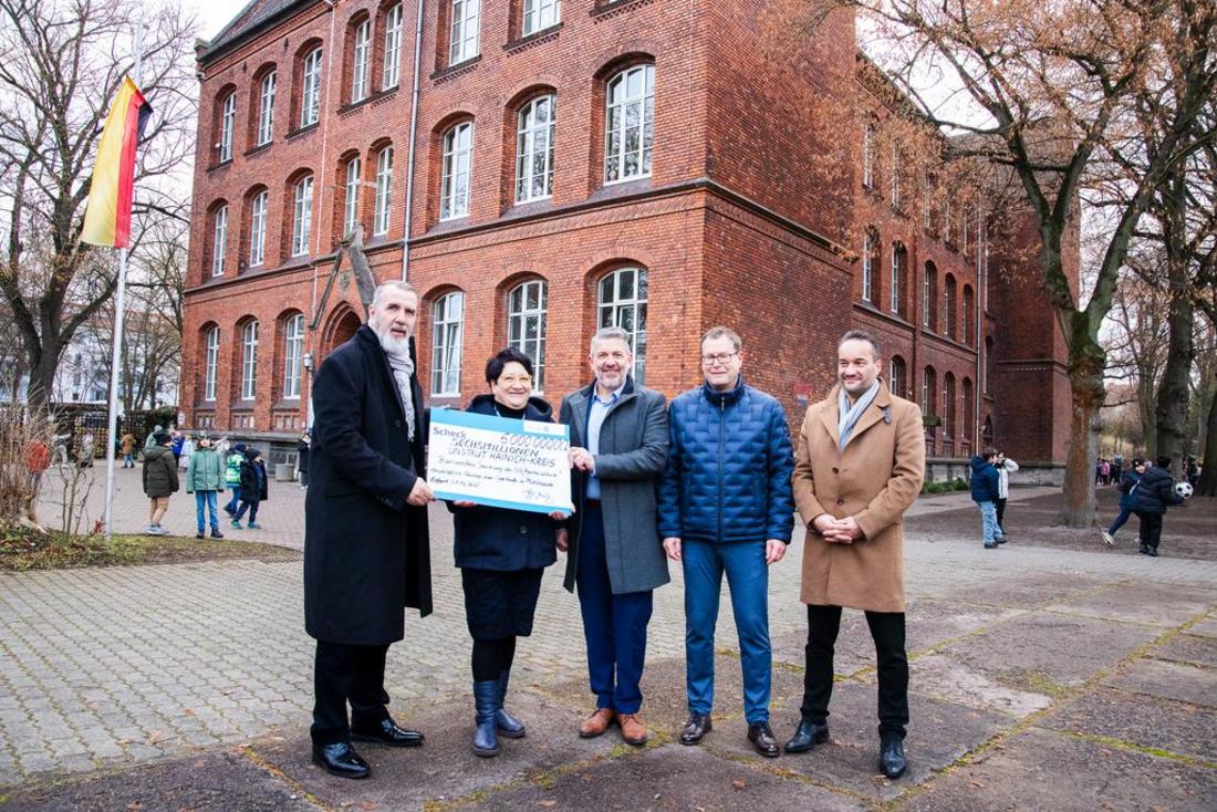 Minister Steffen Schütz steht gemeinsam mit drei weiteren Herren und der Schulleiterin der Martinischule vor dem alten Klinker Schulgebäude und überreicht einen Fördermittelscheck über 6 Millionen Euro
