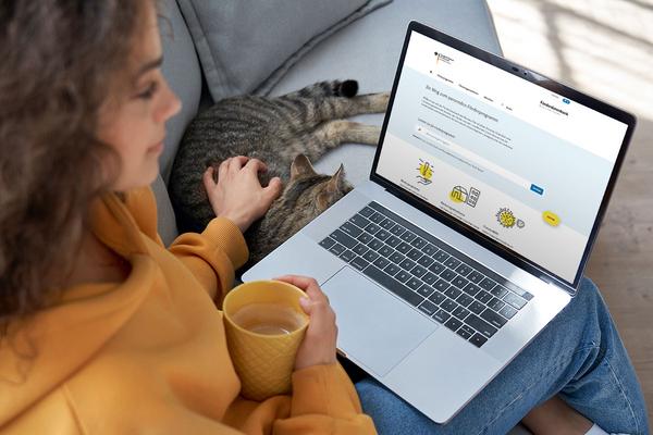 junge Frau sitzt auf dem Sofa, trinkt einen Tee und surft auf der Website des TMDI, sie streichelt nebenbei ihre Katze