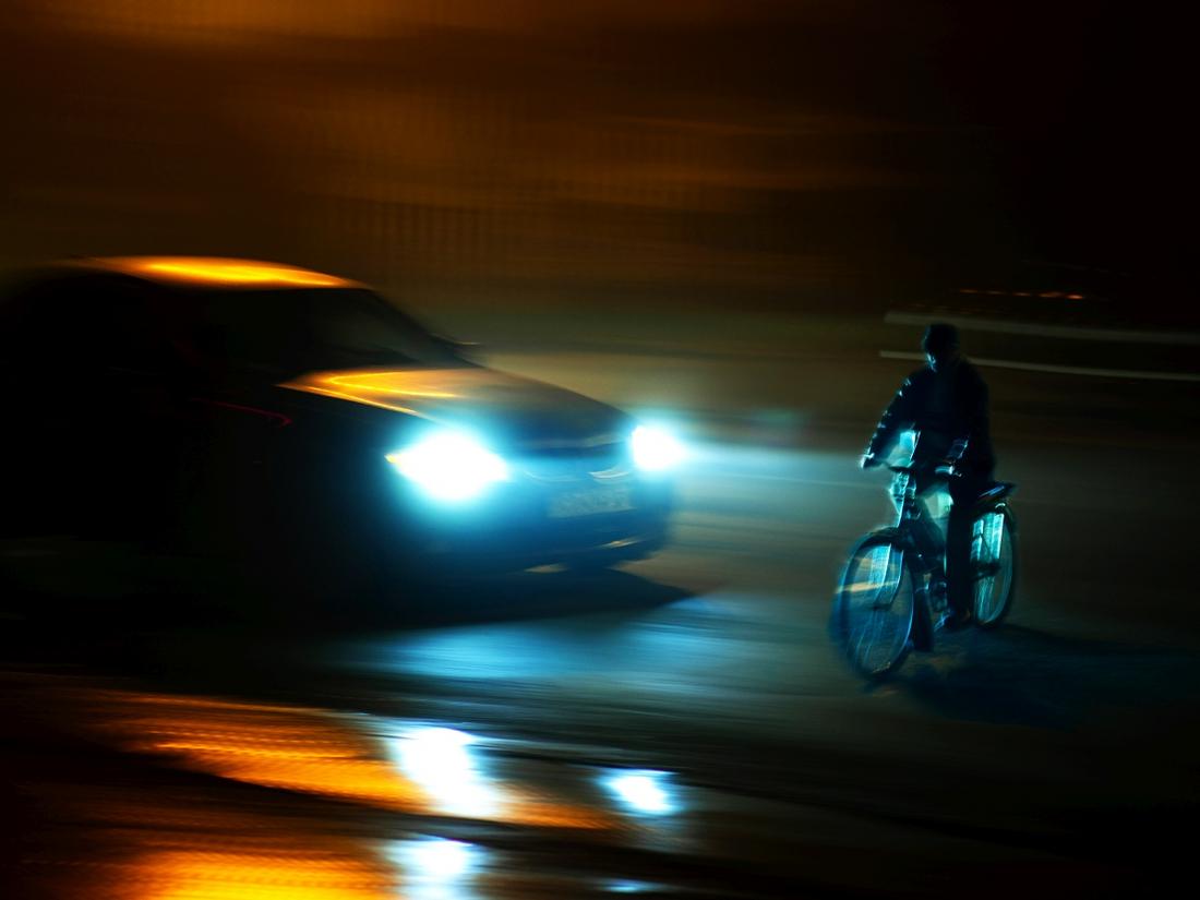 Ein Fahrradfahrer wird von einem Autp in der Dunkelheit angeleuchtet