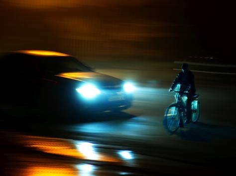 Ein Fahrradfahrer wird von einem Autp in der Dunkelheit angeleuchtet