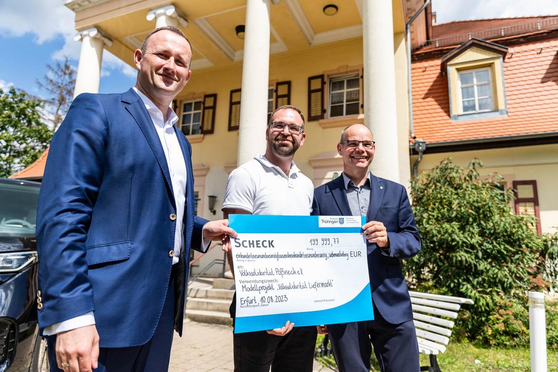 V. l. n. r.: Christian Herrgott (Vorstandsvorsitzender der Volkssolidarität Pößneck) und Marcel Scheibe (lokaler Einzelhändler) erhalten den symbolischen Scheck von Staatsekretär Torsten Weil