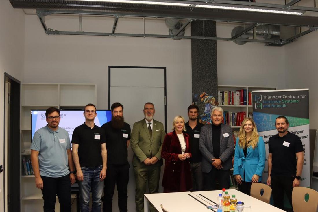 Eine Gruppe Personen steht gemeinsam mit Minister Steffen Schütz und Frau Dr. Sinemus sowie Staatssekretärin Milen Starke in einem Raum des Thüringer Zentrums für Lernende Systeme und Robotik