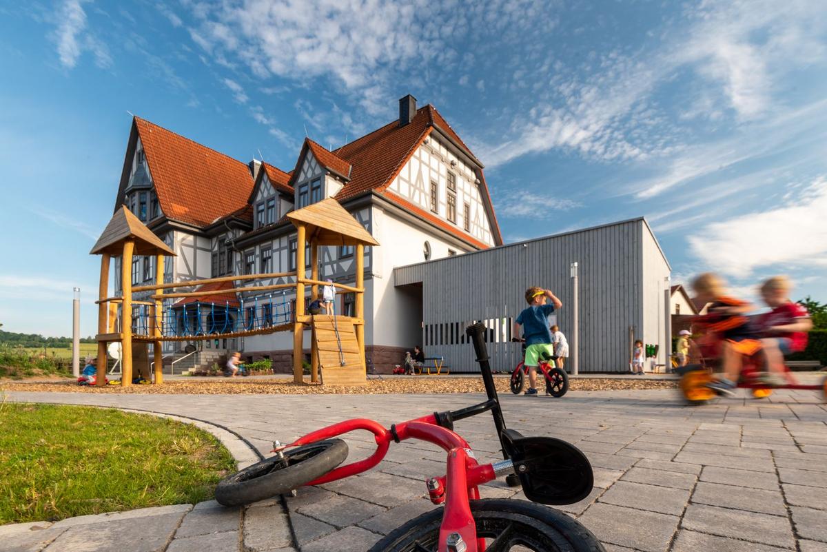 Großes, saniertes Fachwerkhaus mit Spielgeräten im Vordergrund und spielenden Kindern