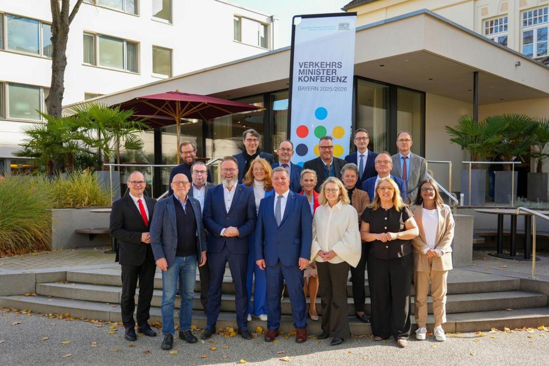 Eine Gruppe Menschen steht anlässlich der Verkehrsministerkonferenz 2025 vor dem Bayerisches Staatsministerium für Wohnen, Bau und Verkehr und lächelt freundlich